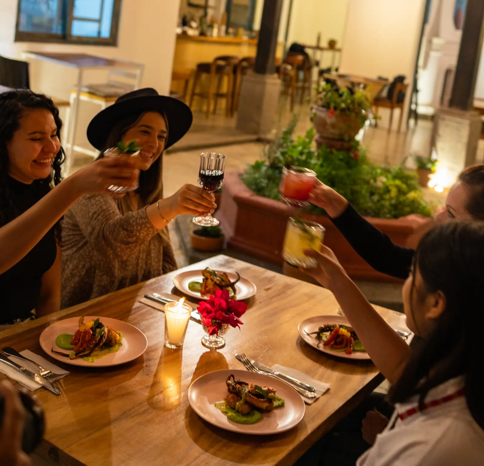 Friends toasting with cocktails over shared plates at a table inside Rosanta