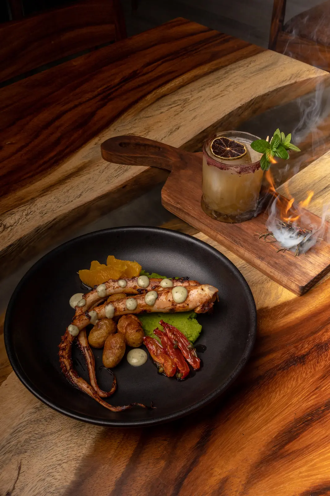 Grilled octopus with roasted potatoes, next to a smoking cocktail on a wooden board, at Rosanta in Antigua Guatemala