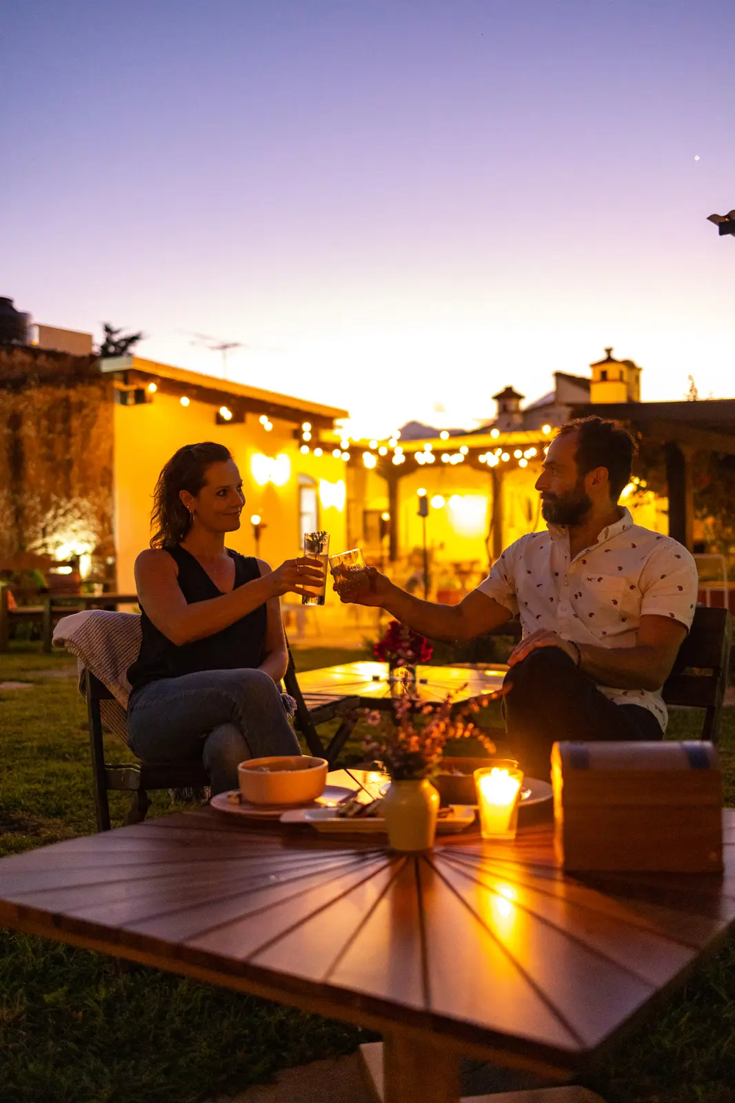 A couple toasting at dusk in the Rosanta garden, with string lights and the colonial rooftops of Antigua behind them