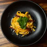 House-made fettuccine with confit tomatoes and a basil leaf on a black plate